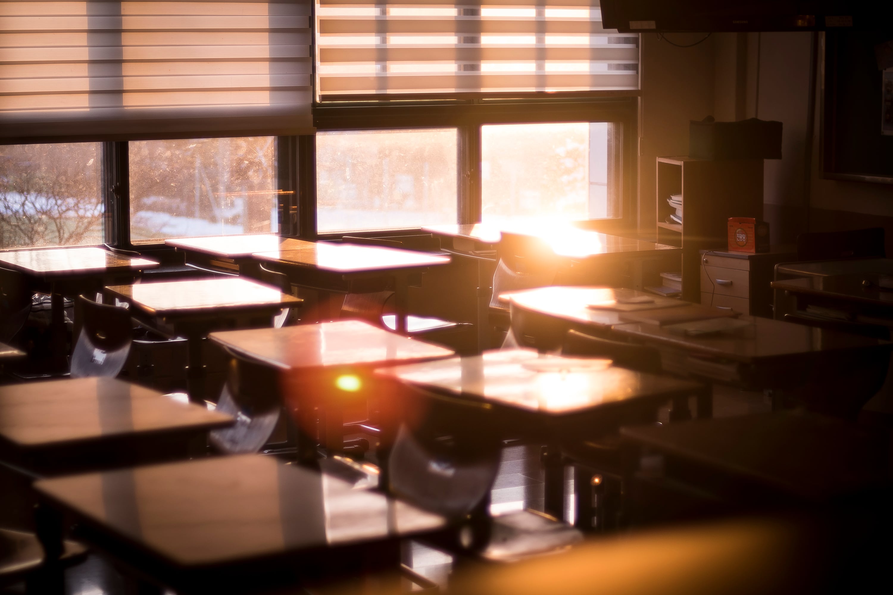 A bright warm light from the sun shines through a classroom window onto students' desks.
