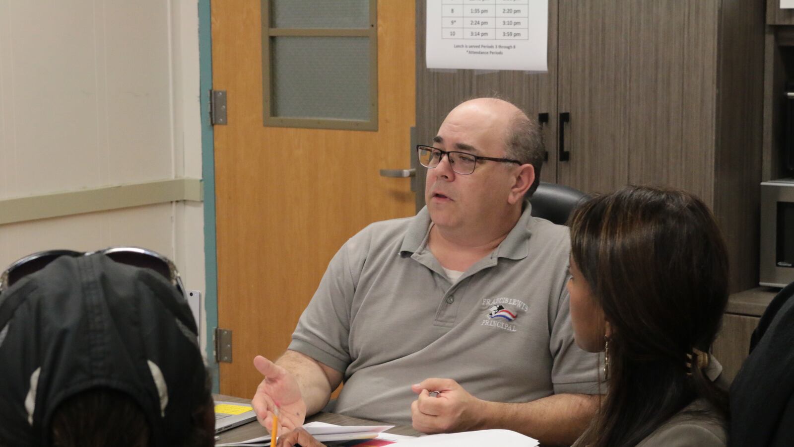 A man in a taupe polo shirt sits at a table.