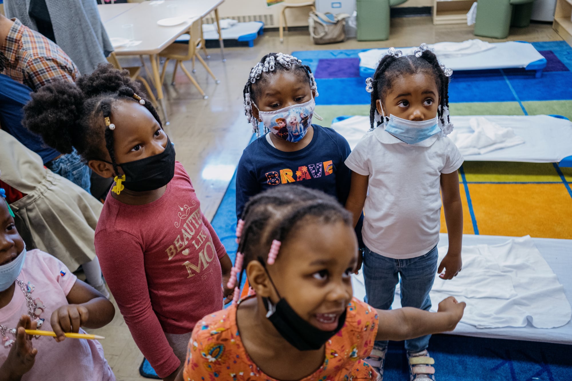 four girls with braids wearing masks over mouth or chin stand in a cluster as one girl dances and