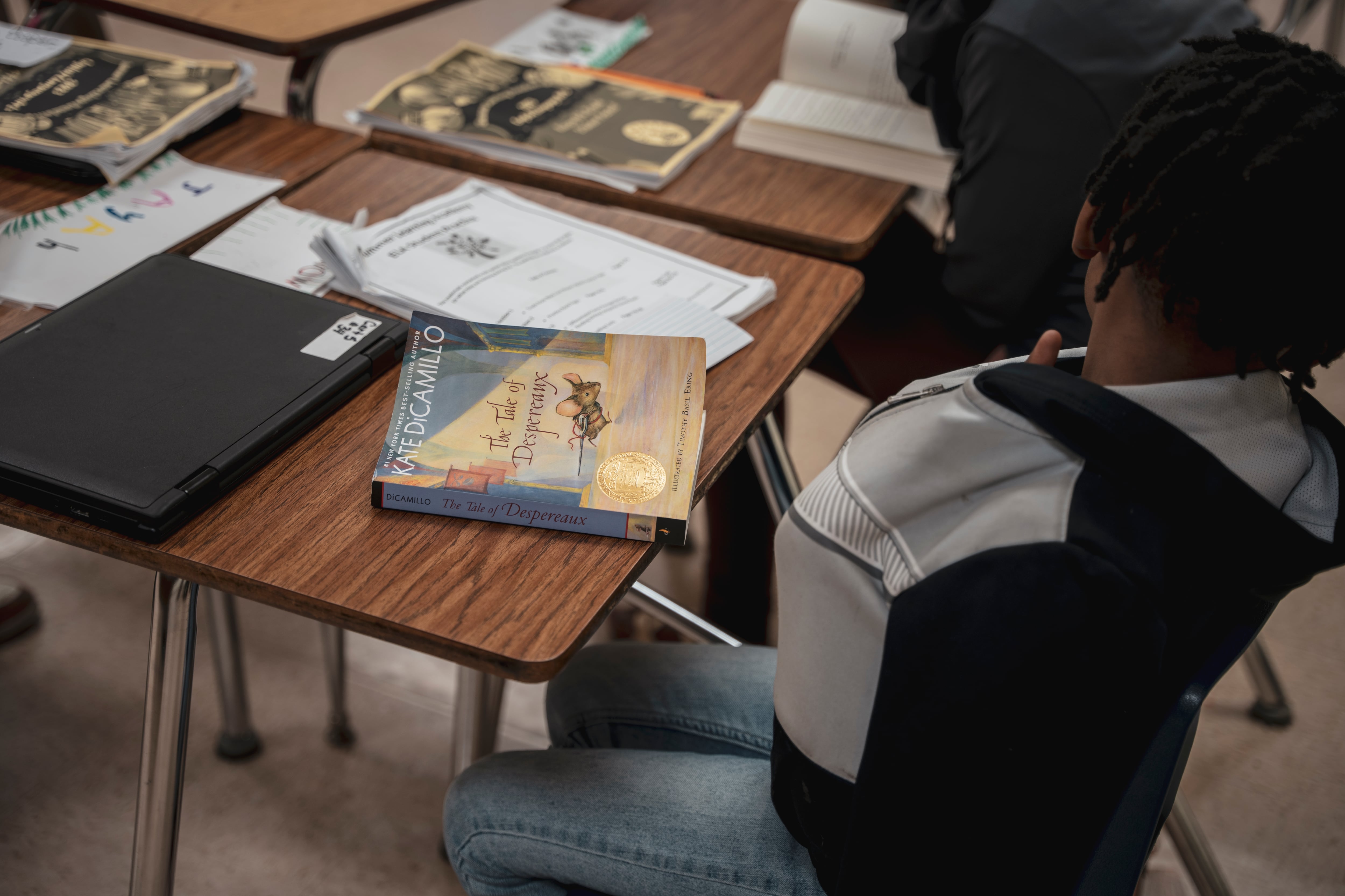 A book and papers sit on a desk in front of a male student.