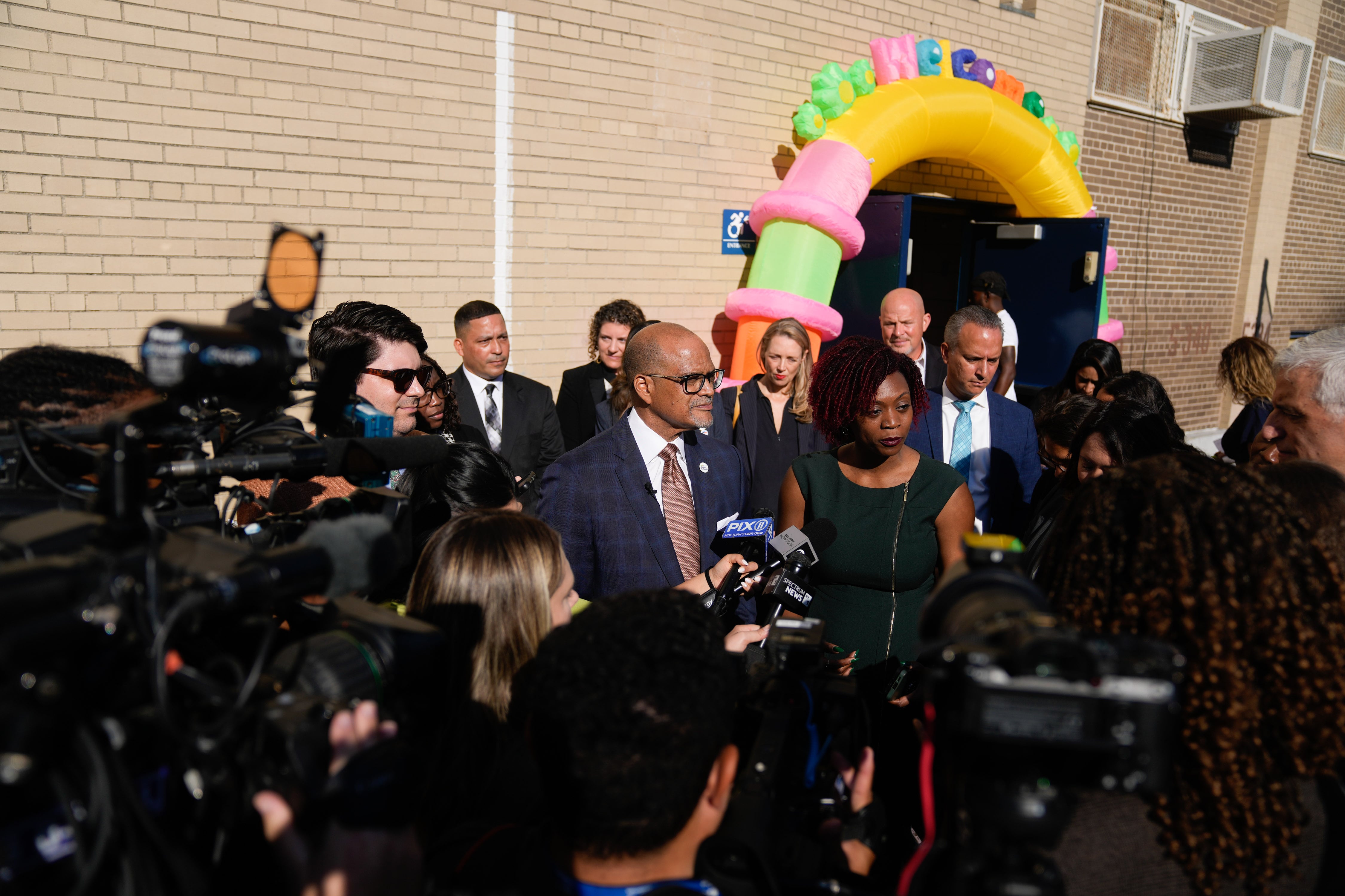 A man in a suit is surrounded by a gaggle of reporters with cameras.