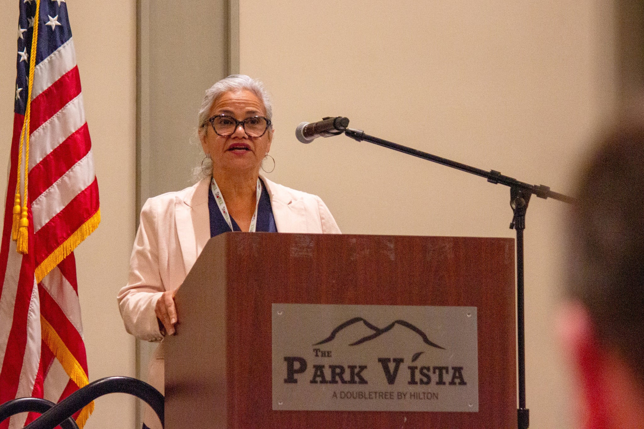 A woman wearing a white jacket and glasses standing behind a podium labeled “The Park Vista”