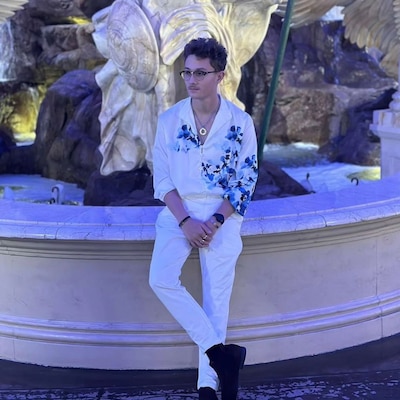 A person wearing white pants and blouse sits on a stone ledge posing for a portrait.