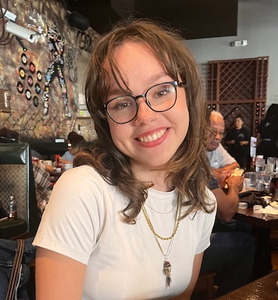 Headshot of a young woman with brown hai, wearing a white shirt and glasses.