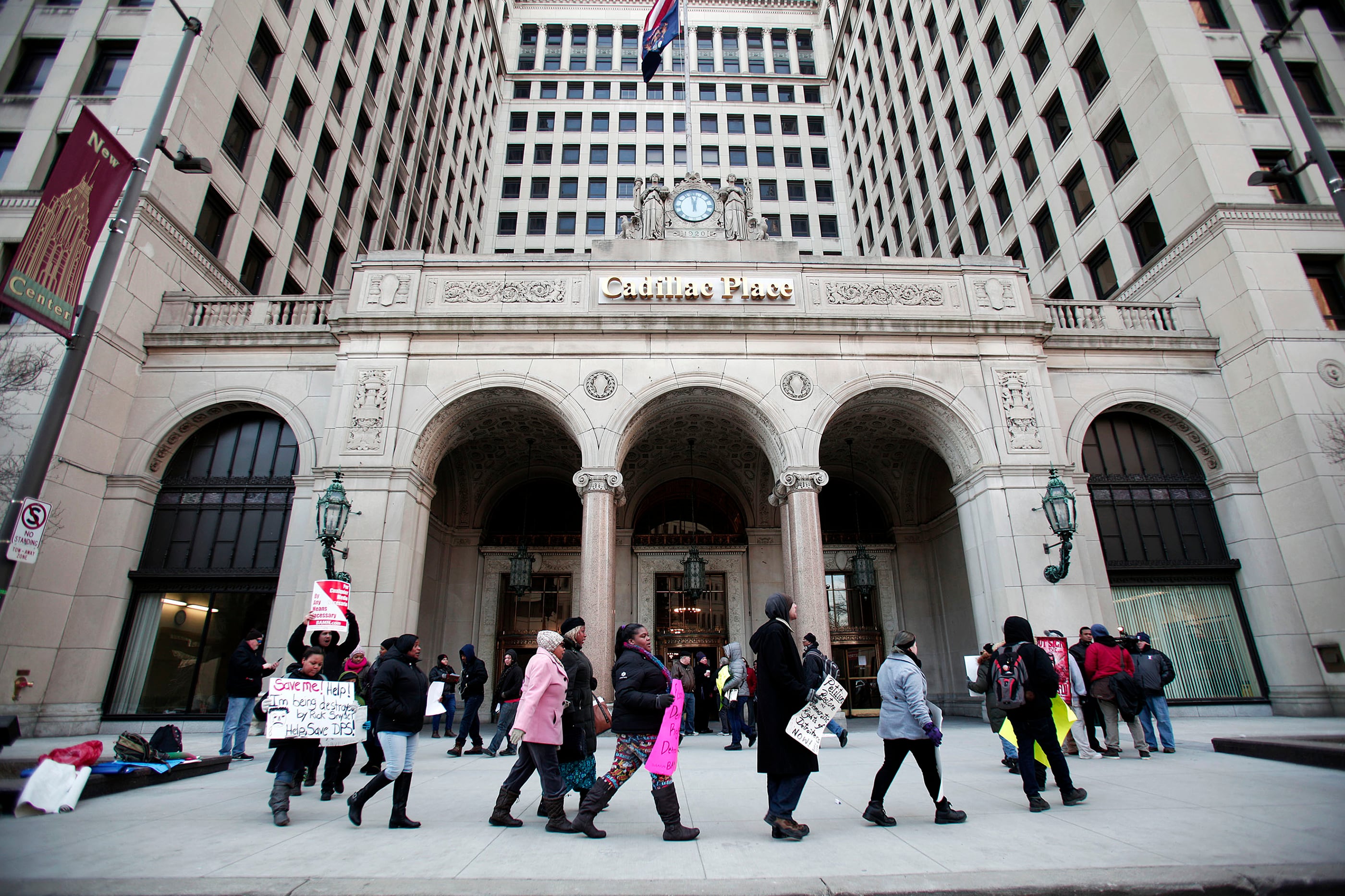 A photograph of a line of adults protesting in a circle outside of a large stone building on a grey, cold day.