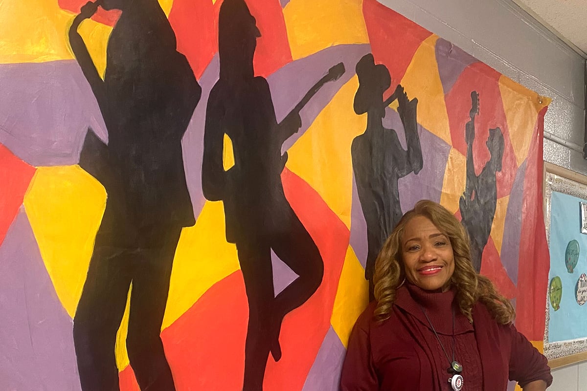 A woman with a burgundy top stands in front of a mural.