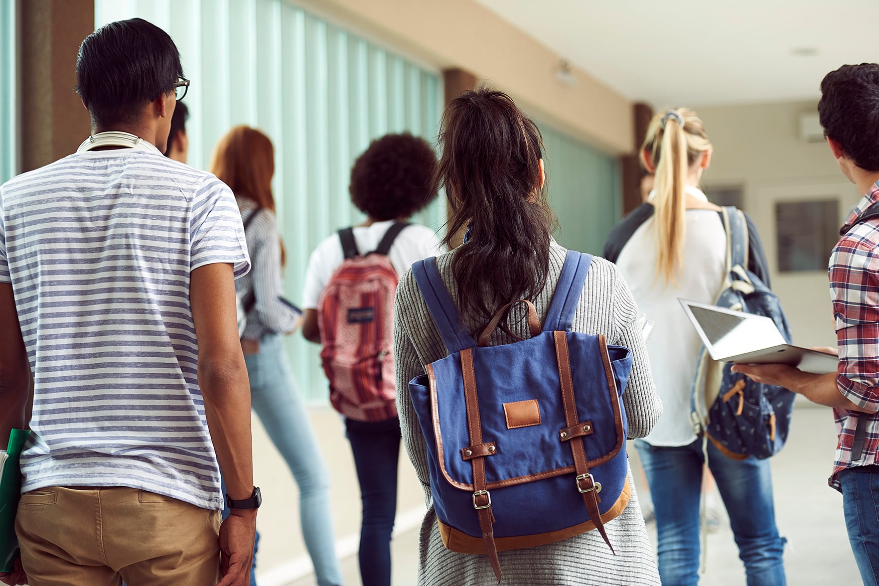 High school students wearing backpacks walk down a school hallway.
