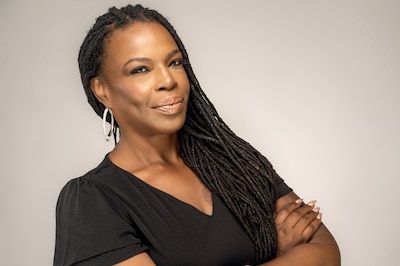 A photograph of a Black woman with long dark hair wearing a black shirt posing for a portrait.