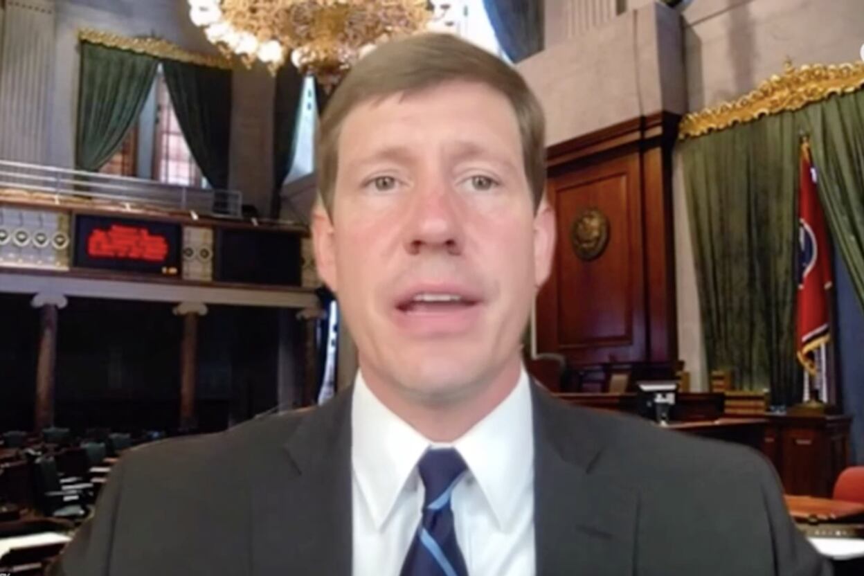 Man in suit and tie speaks in a legislative chamber.