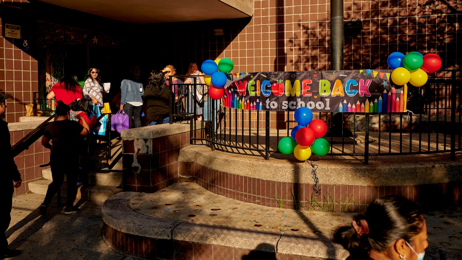 A sign reads “Welcome Back to School” outside of a large brick building as students walk into its doors.