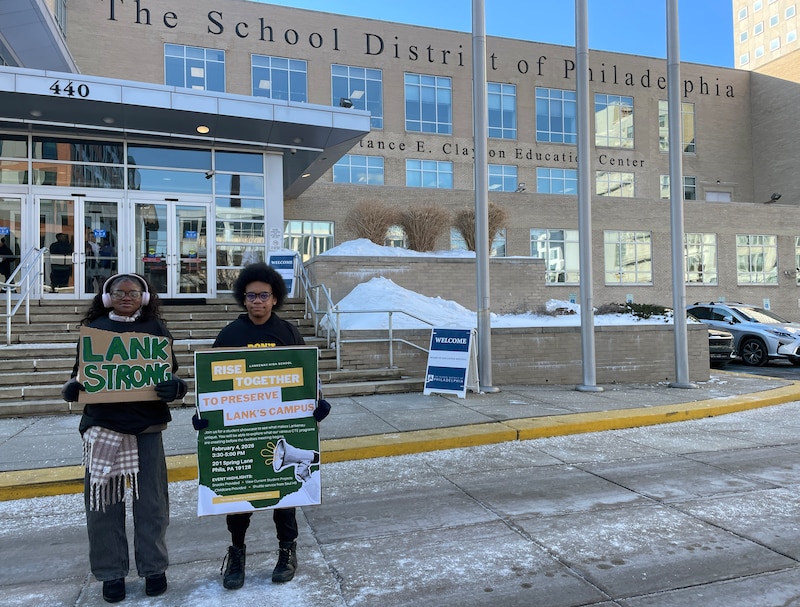 A photograph of two students holding signs during a protest outside.