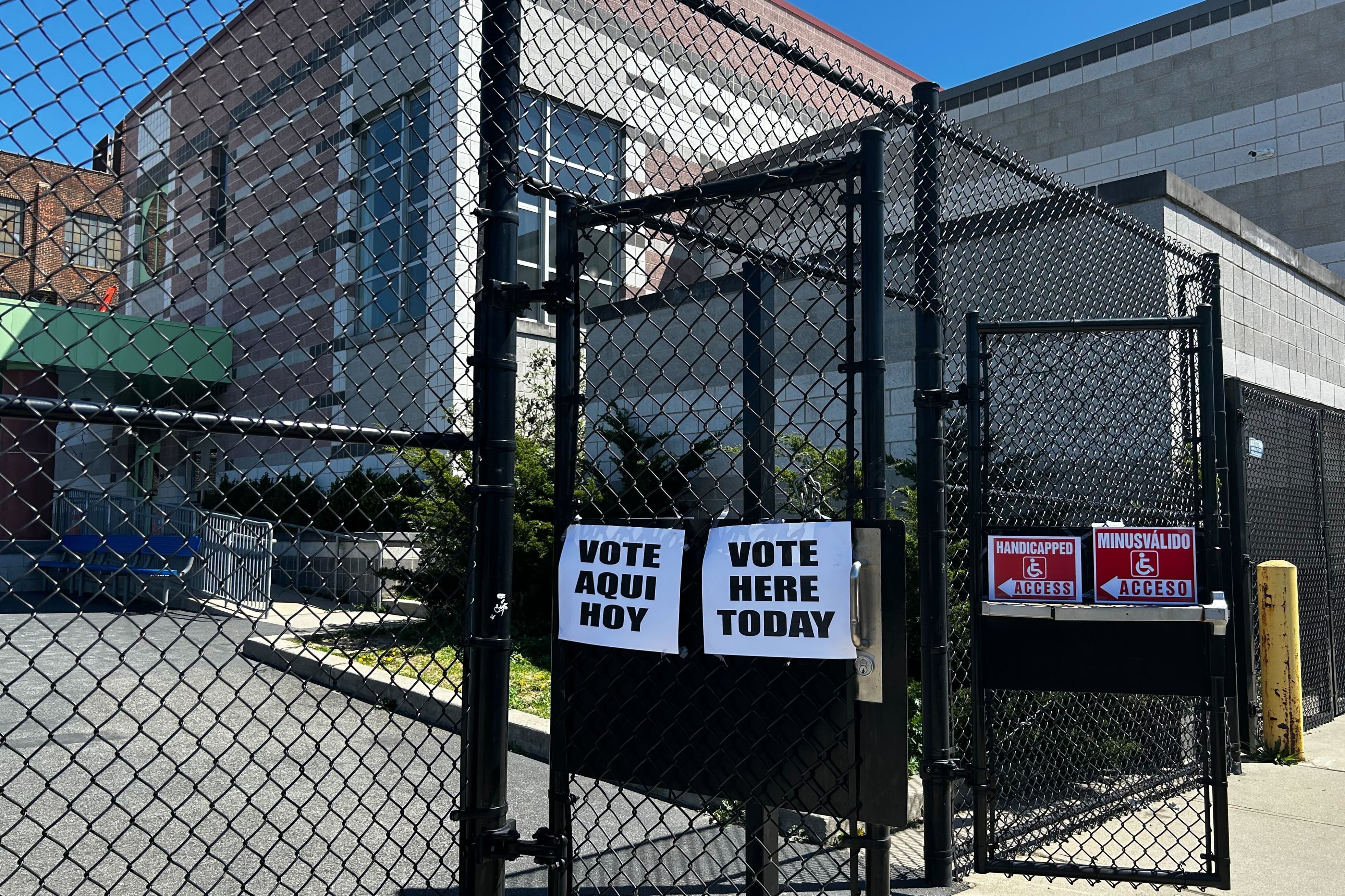 A fence with voting information on it in front of a brick building.
