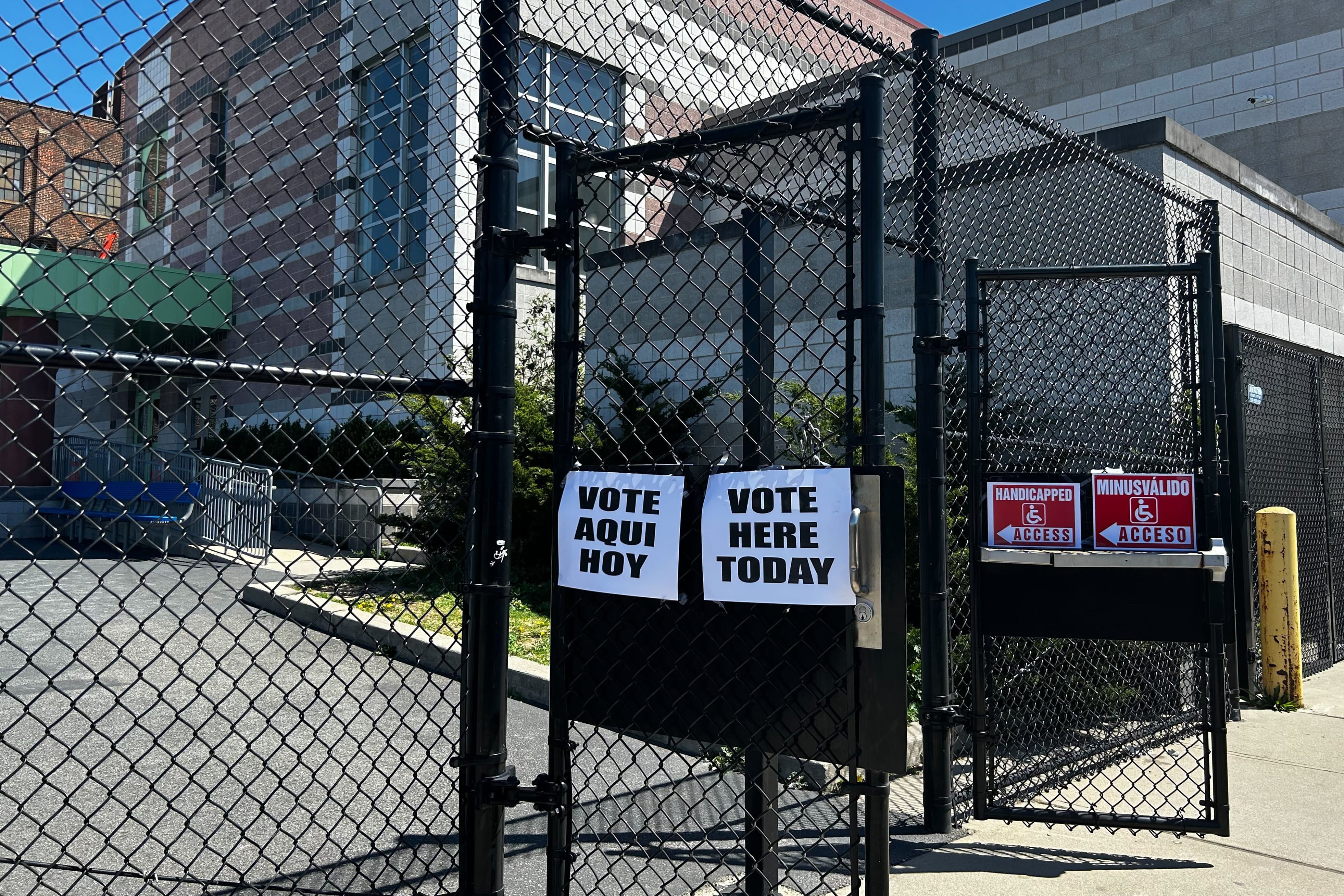A fence with voting information on it in front of a brick building.