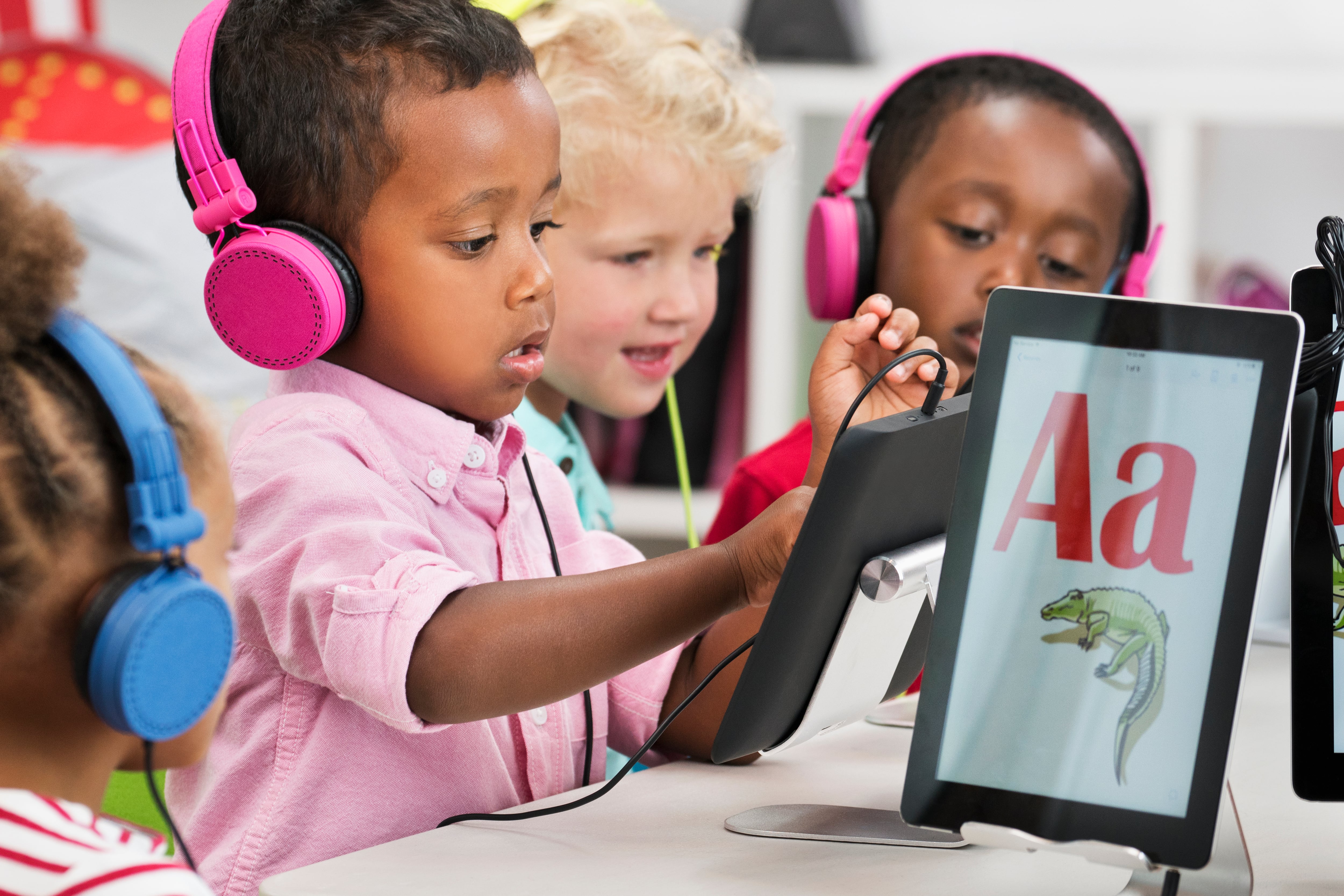 A photograph of students learning alphabet with digital tablets in a classroom.