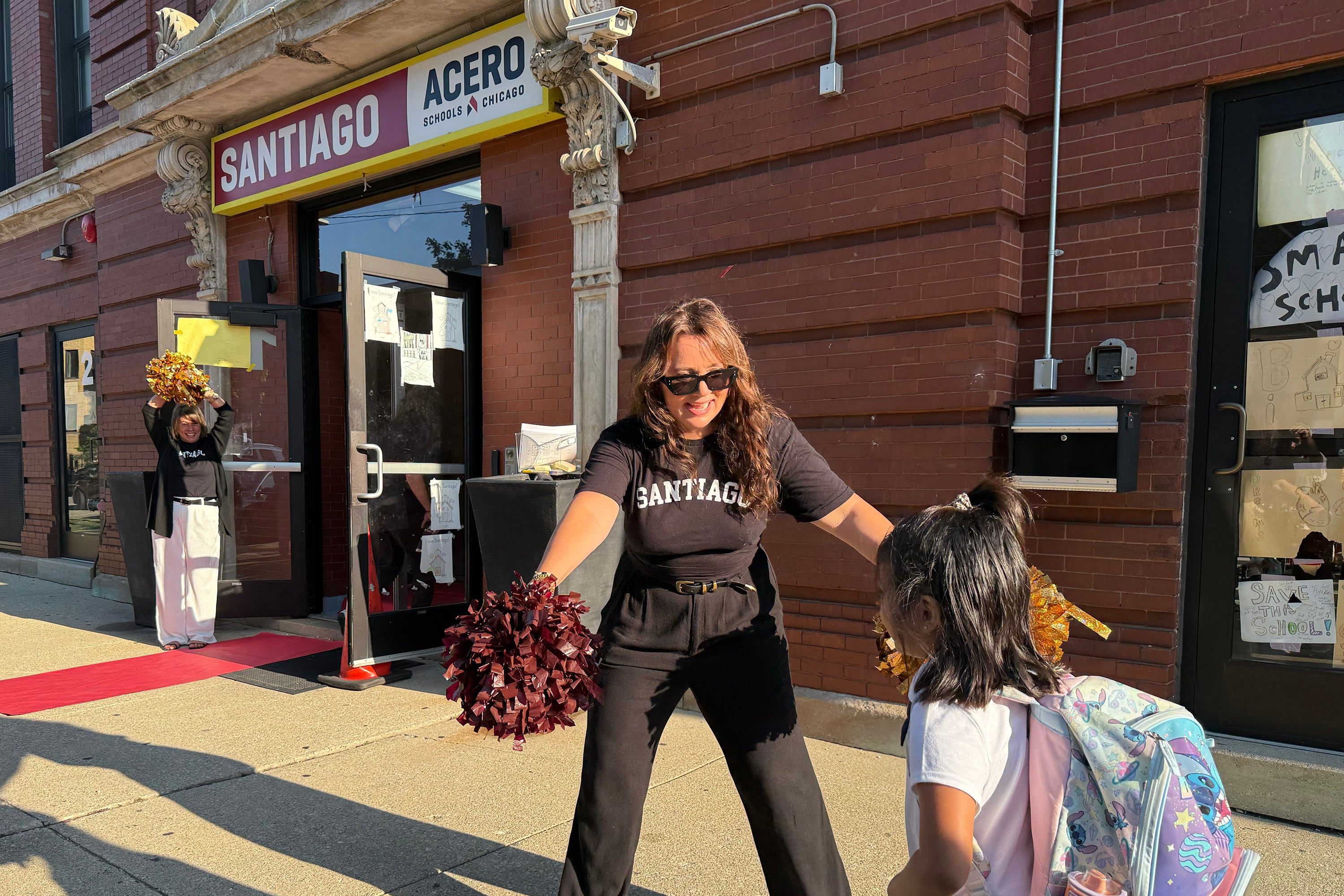 A photograph of adults and students greeting each other outside of a brick school building.