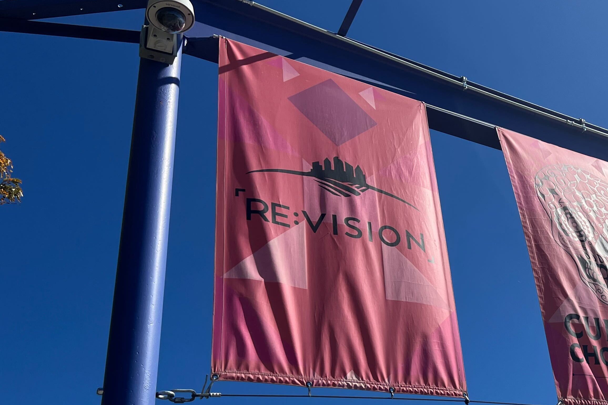 A photograph of a red flag with the word "RE:Vision" with a blue sky in the background.