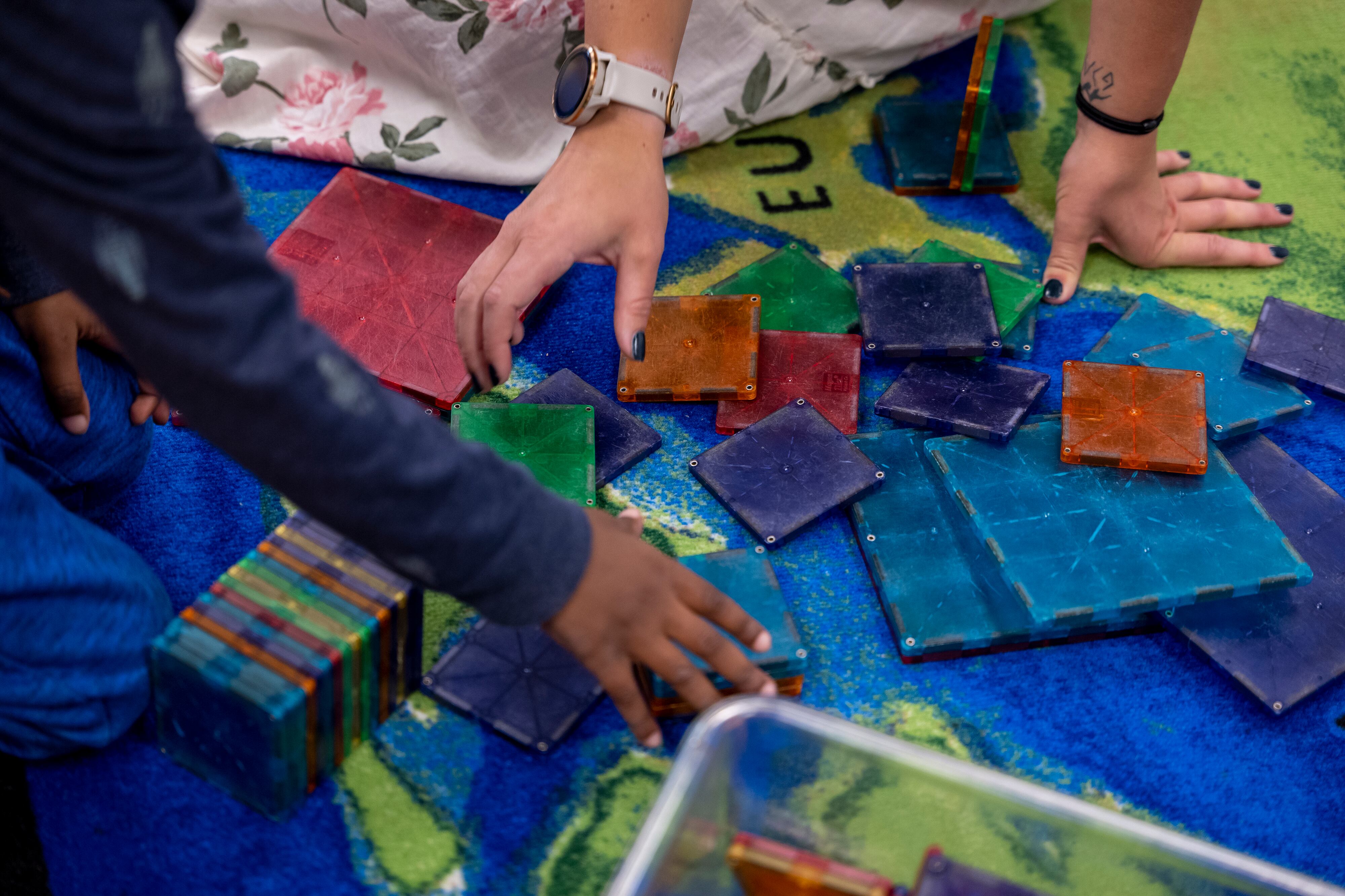 Two sets of hands, one belonging to a teacher and one belonging to a child, play with colorful tiles