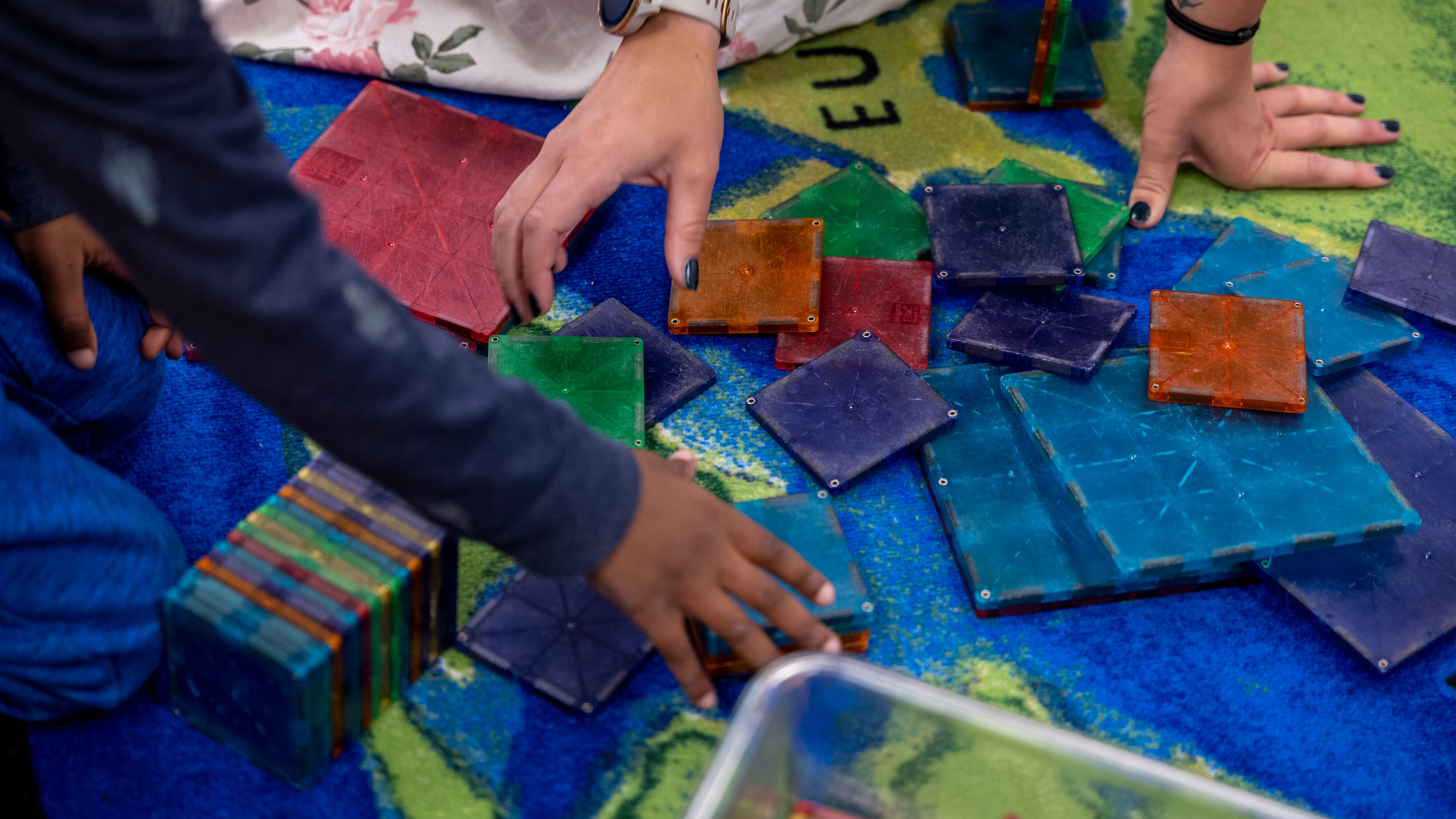 Two sets of hands, one belonging to a teacher and one belonging to a child, play with colorful tiles