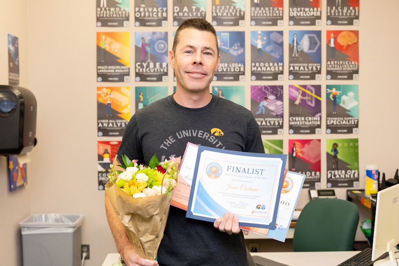 A man in a black t-shirt holds documents and flowers.