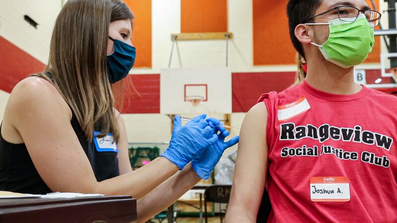 A woman in a mask administers a COVID vaccine to a teenage boy wearing a red Rangeview Social Justice Club T-shirt.