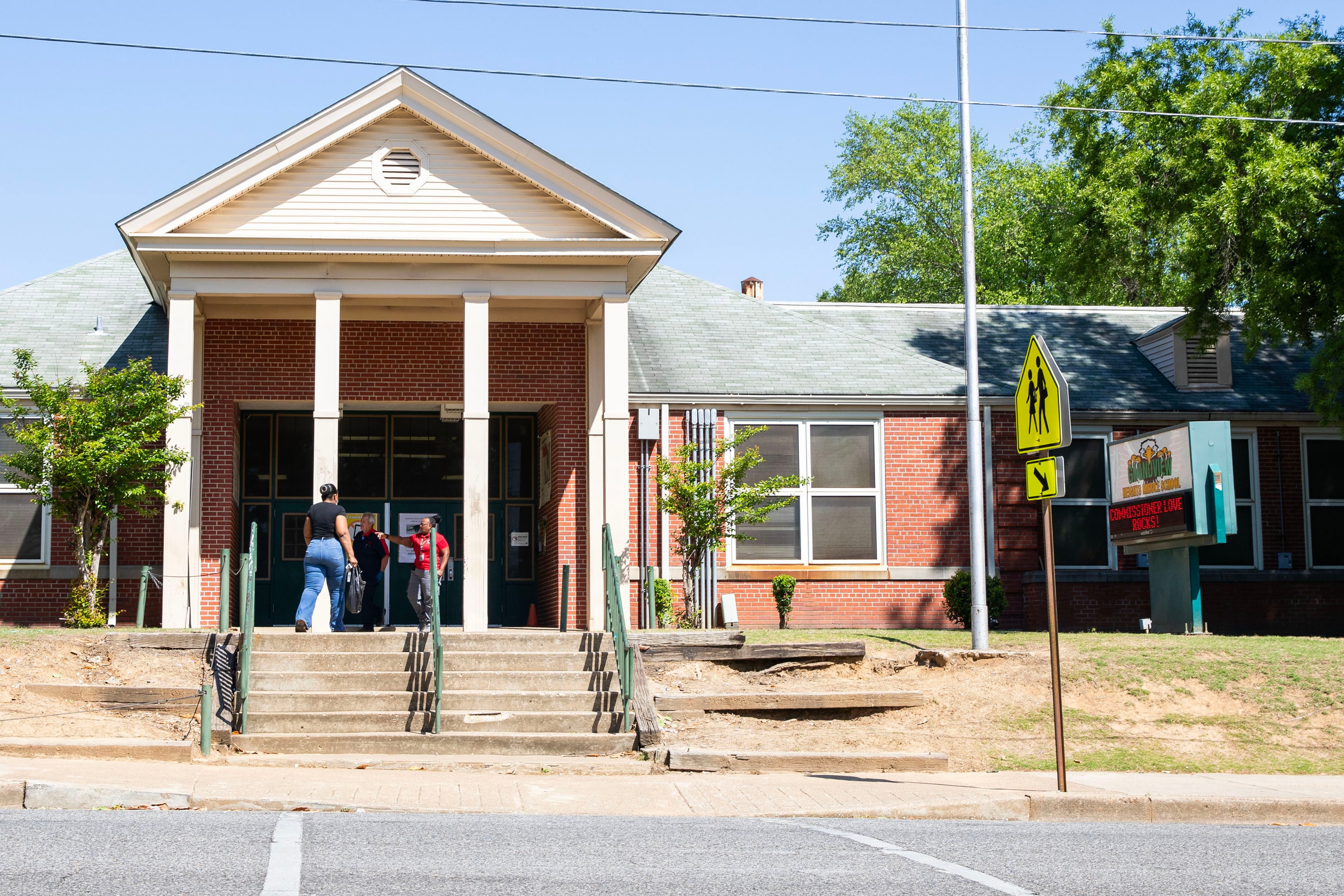 People enter the front entrance of a large brick school building.