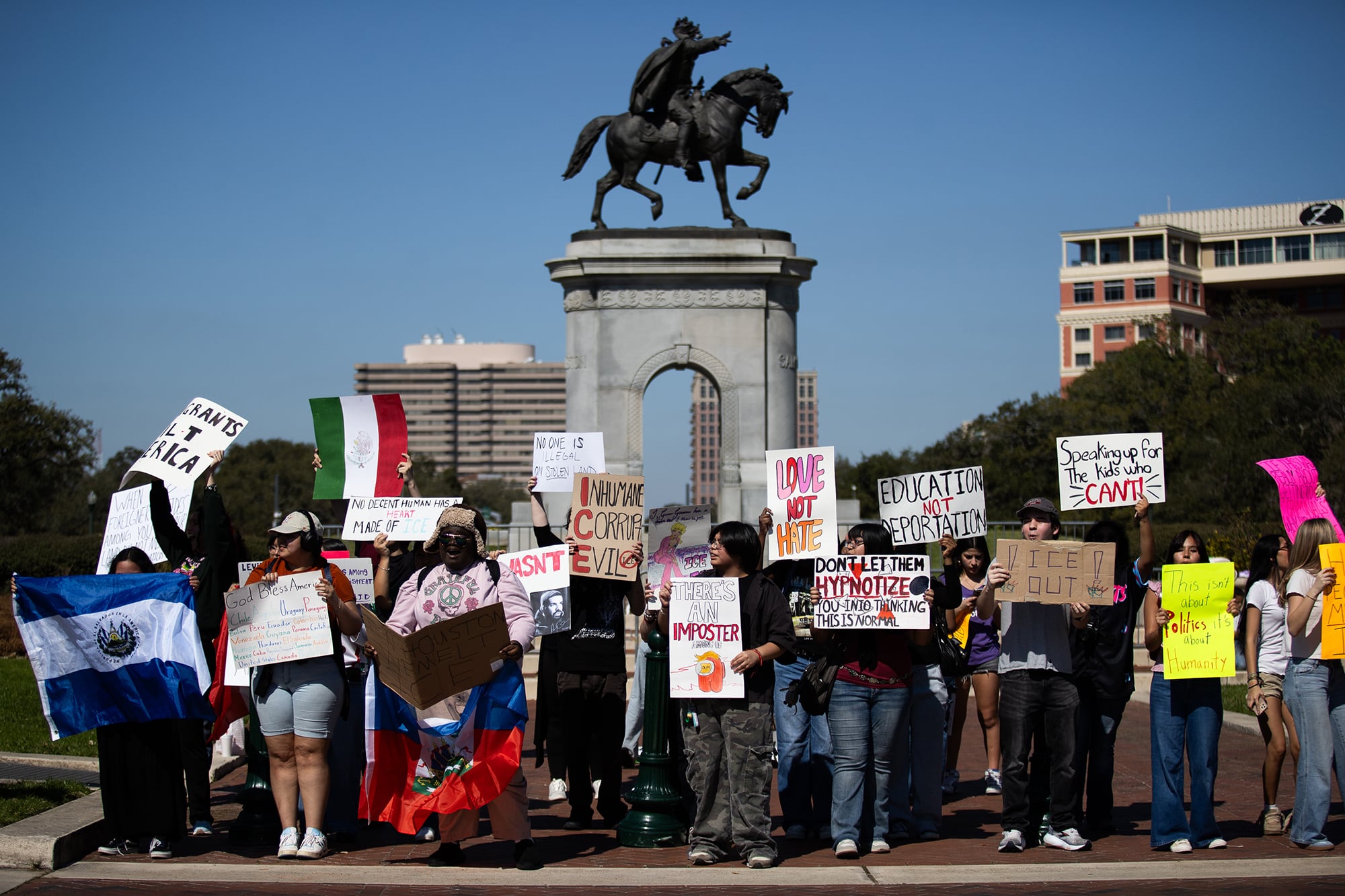 A photograph of a large group of students protesting in front of a statue outside.