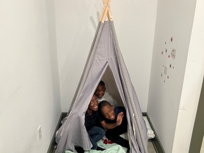 A photograph of three young Black boys playing inside of a cloth tent in a room.