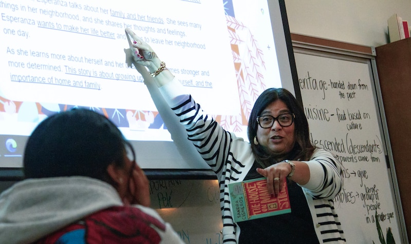 A woman in a striped sweater and glasses points to words on a screen.