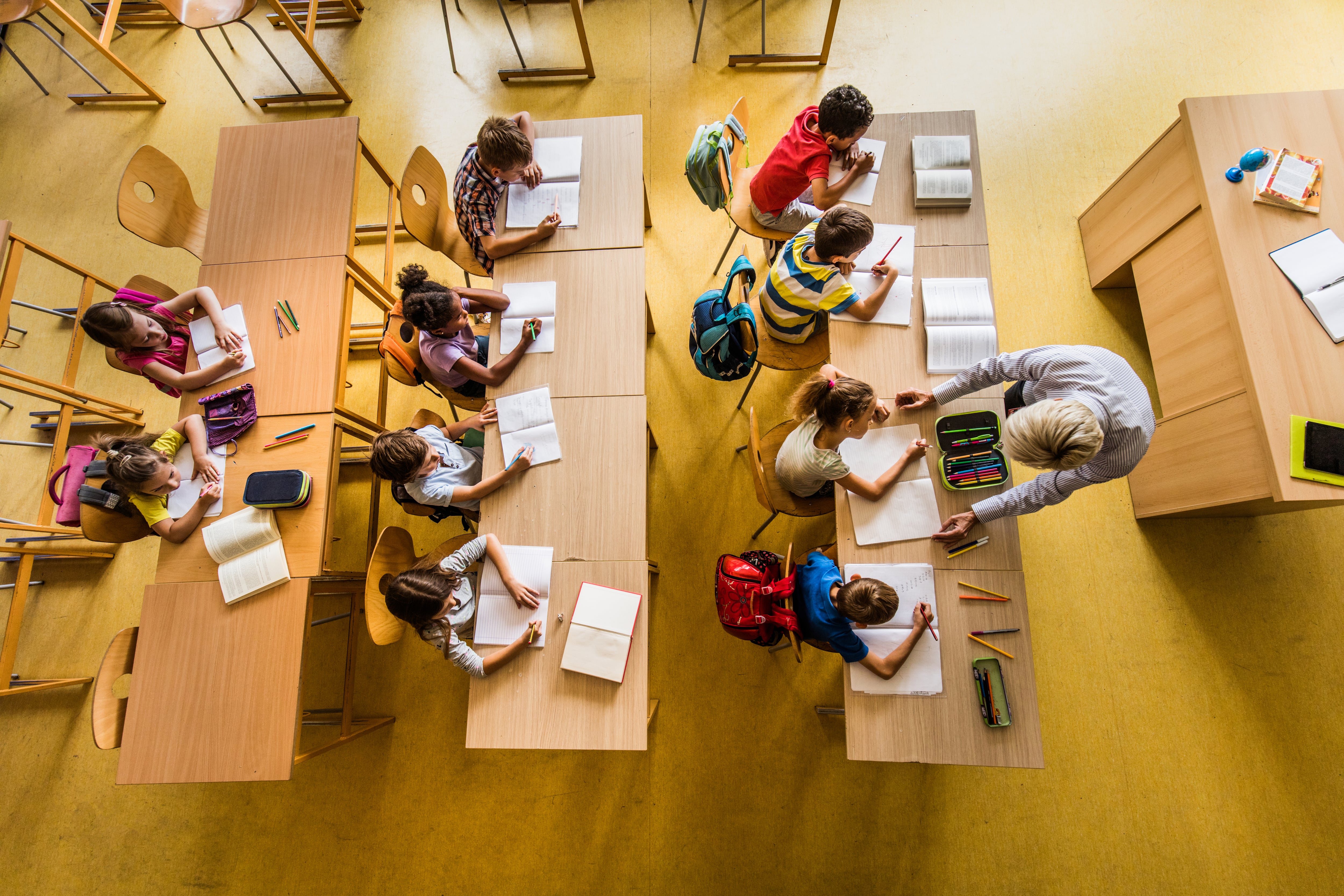 High angle view of large group of elementary students having a class in the classroom. Teacher is assisting one student.