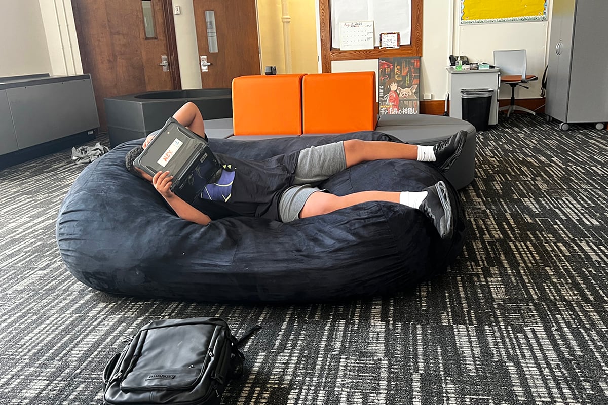 A boy in a black shirt and gray shorts holds a computer on a beanbag chair.