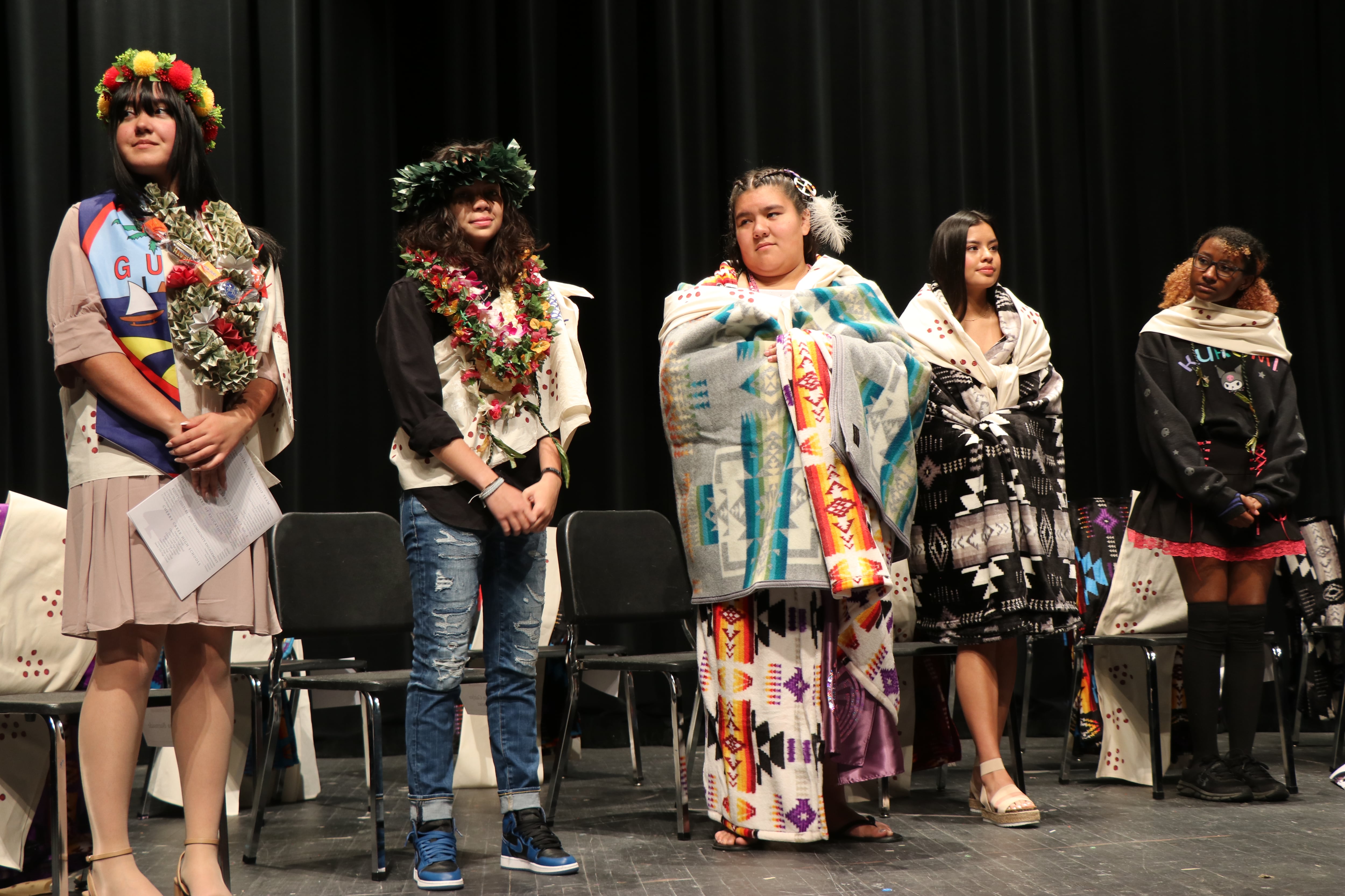 Native American students dressed in colorful traditional regalia during a graduation ceremony.