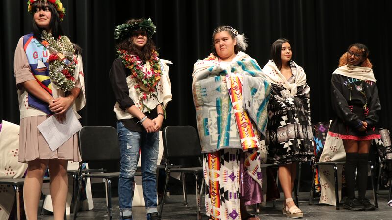 Native American students dressed in colorful traditional regalia during a graduation ceremony.
