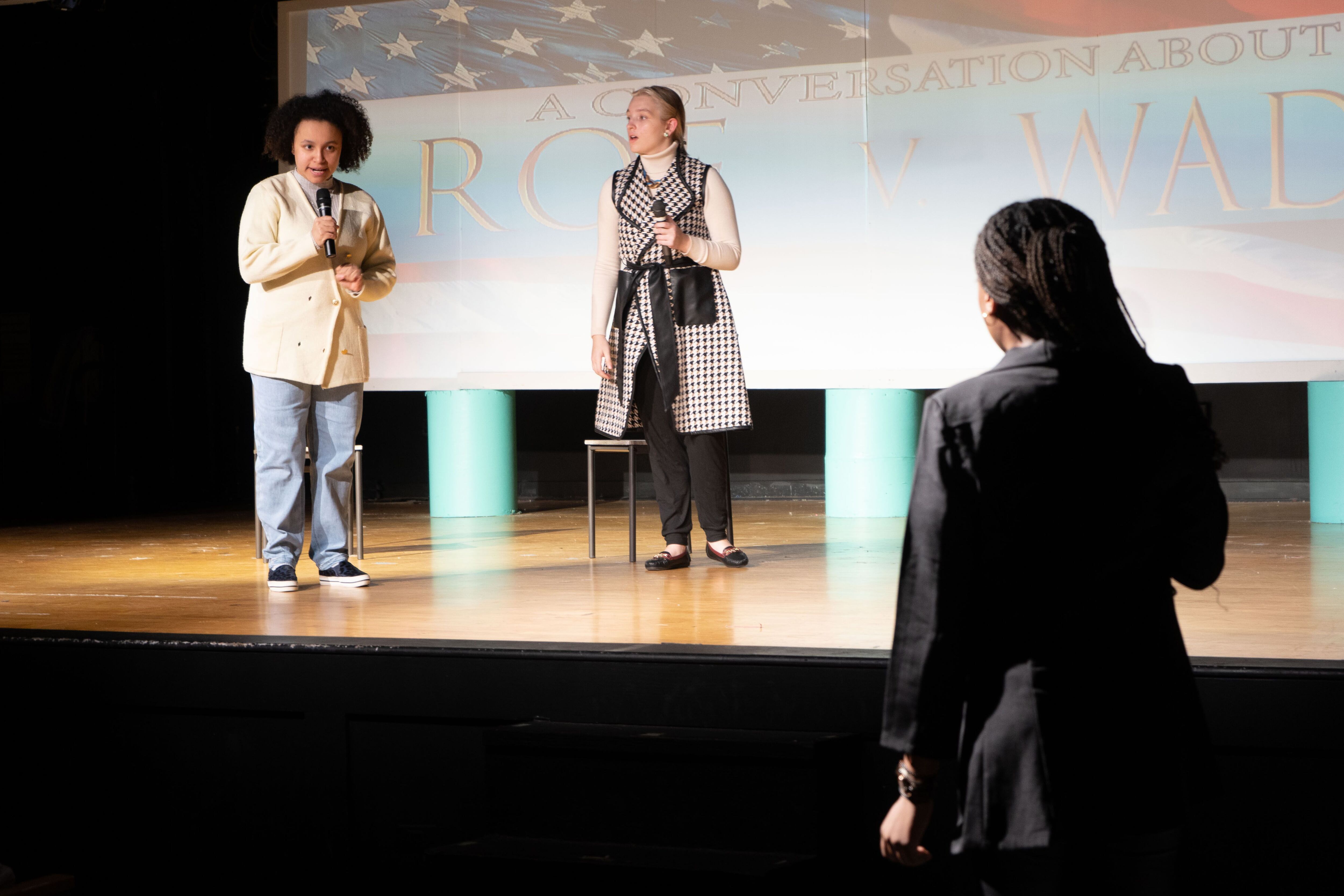 Two people stand on a stage and another stands in front.