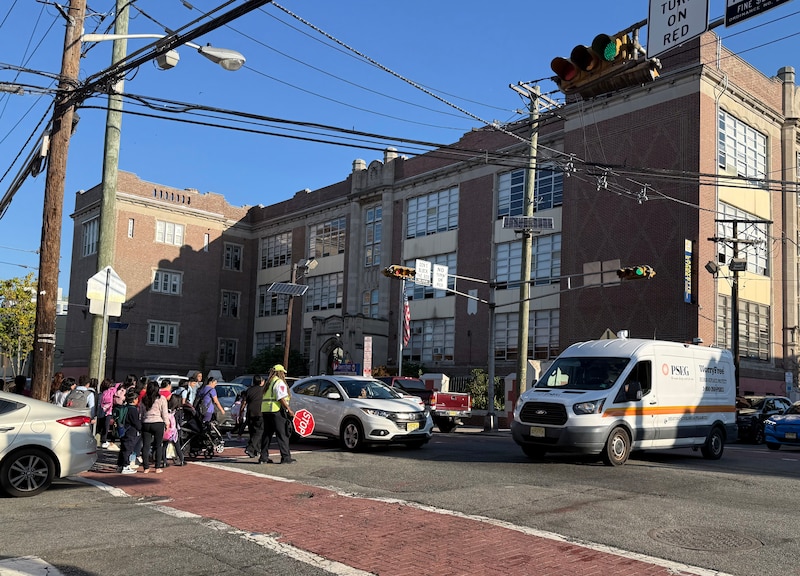 A photograph of a group of people crossing a busy street on a sunny day.