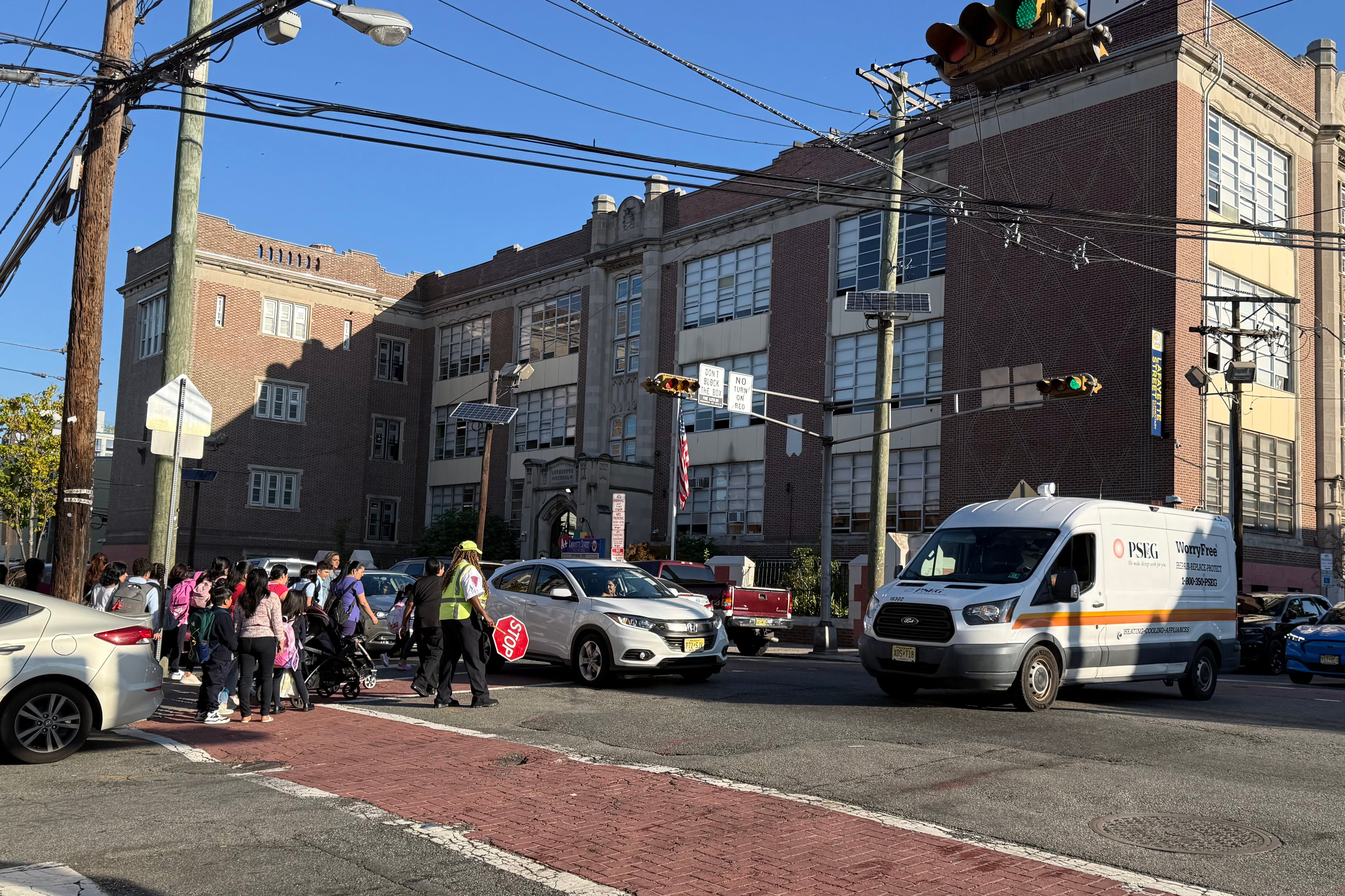 A photograph of a group of people crossing a busy street on a sunny day.