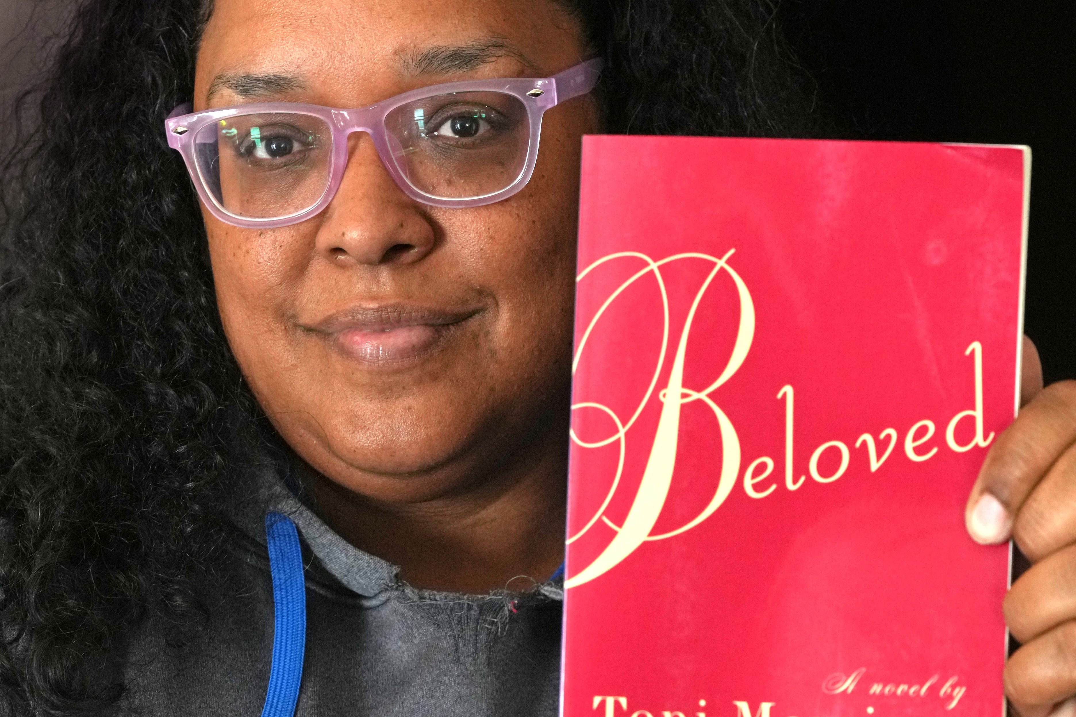 A woman in a gray sweatshirt and glasses holds the book, "Beloved."