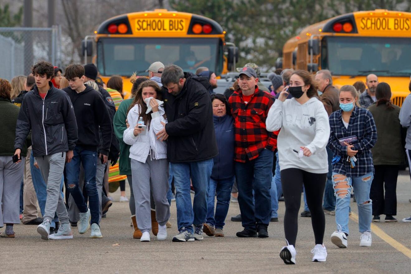 Students and family members walk on a black top as two school busses sit in the background.