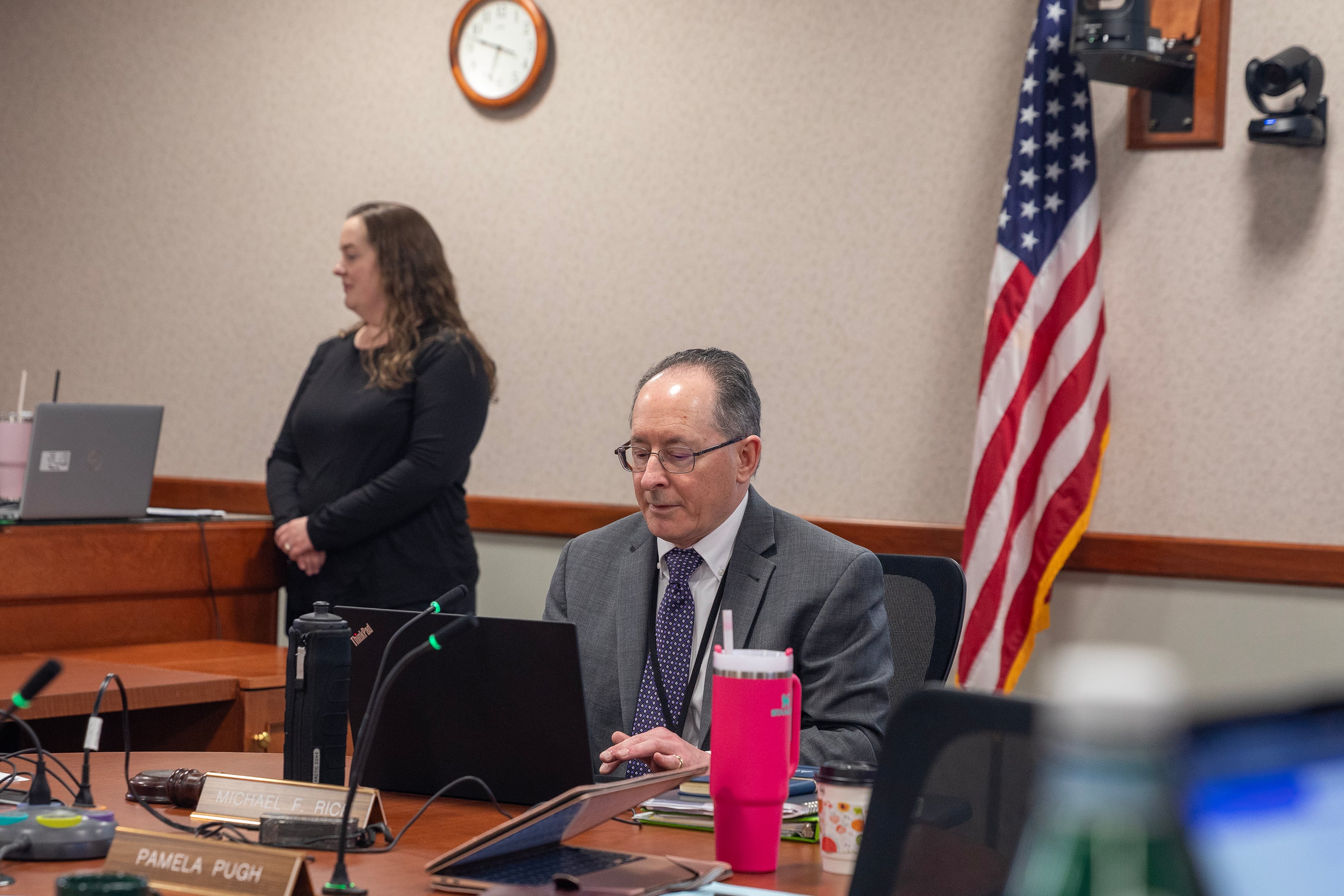 A group of people in business clothes sit at a wooden table in a conference room.