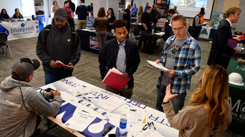 Job candidates stand around a table at a career fair.