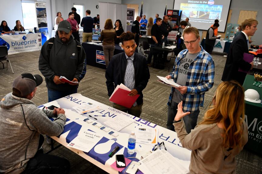 Job candidates stand around a table at a career fair.