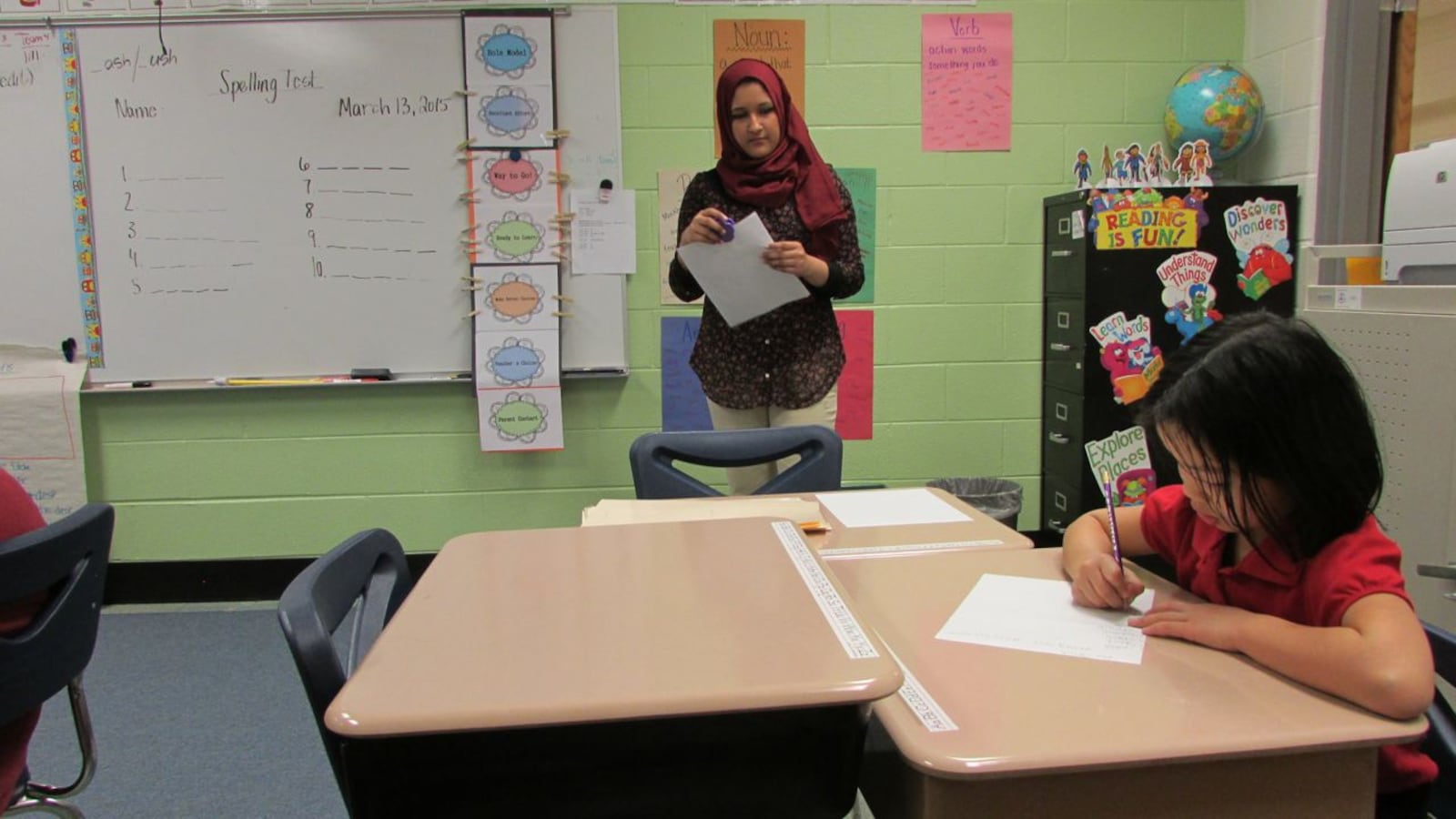 An IPS School 79 student works on a test while her teacher looks on.