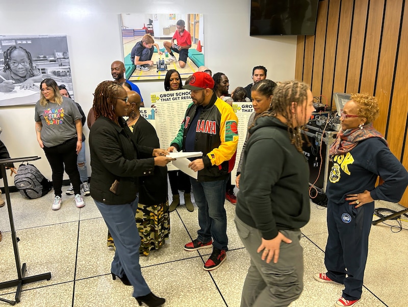 Two people hand out papers to a group of people in the background.