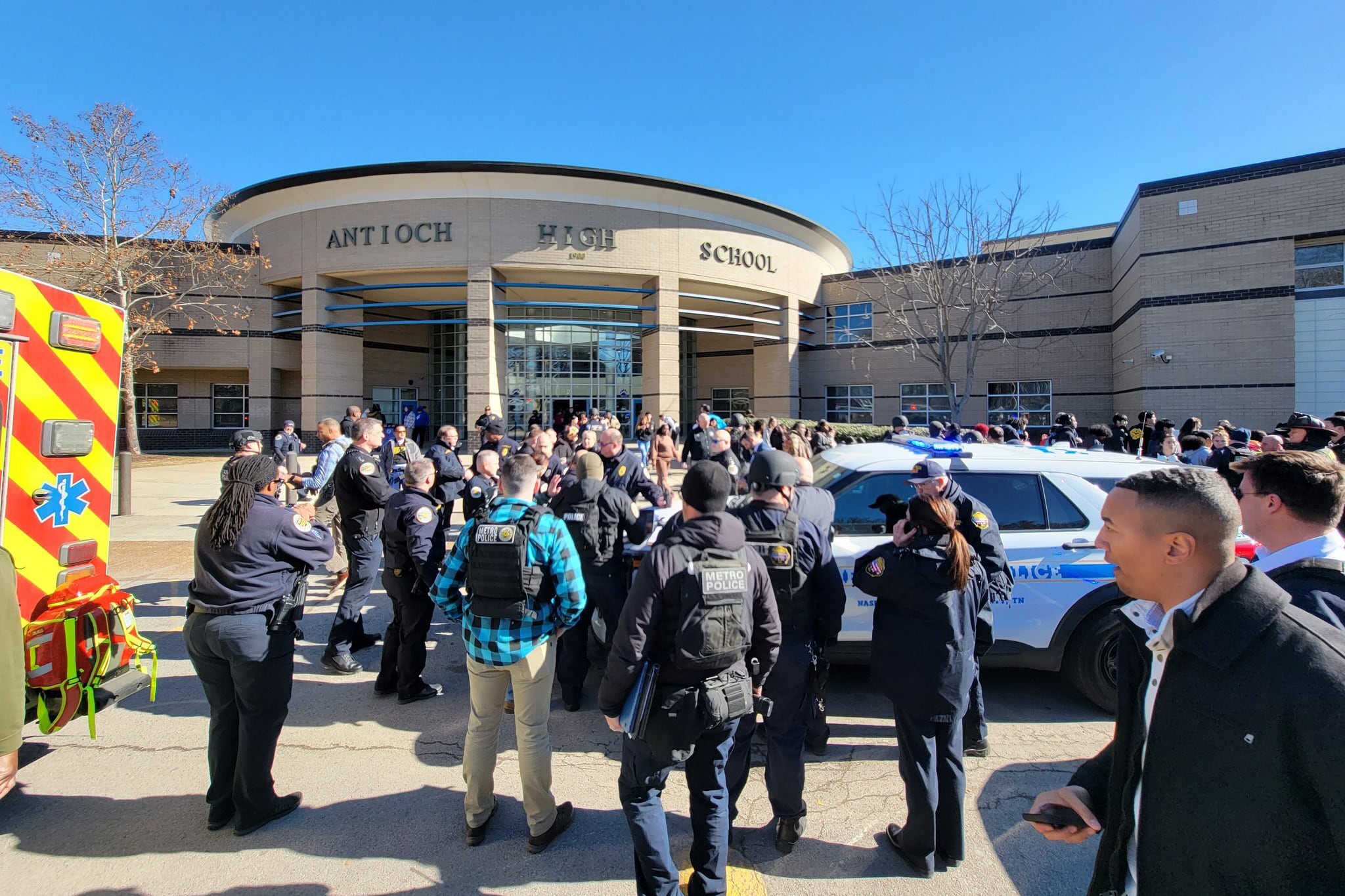 A crowd of adults and mostly emergency and police respondents outside of a large school building.