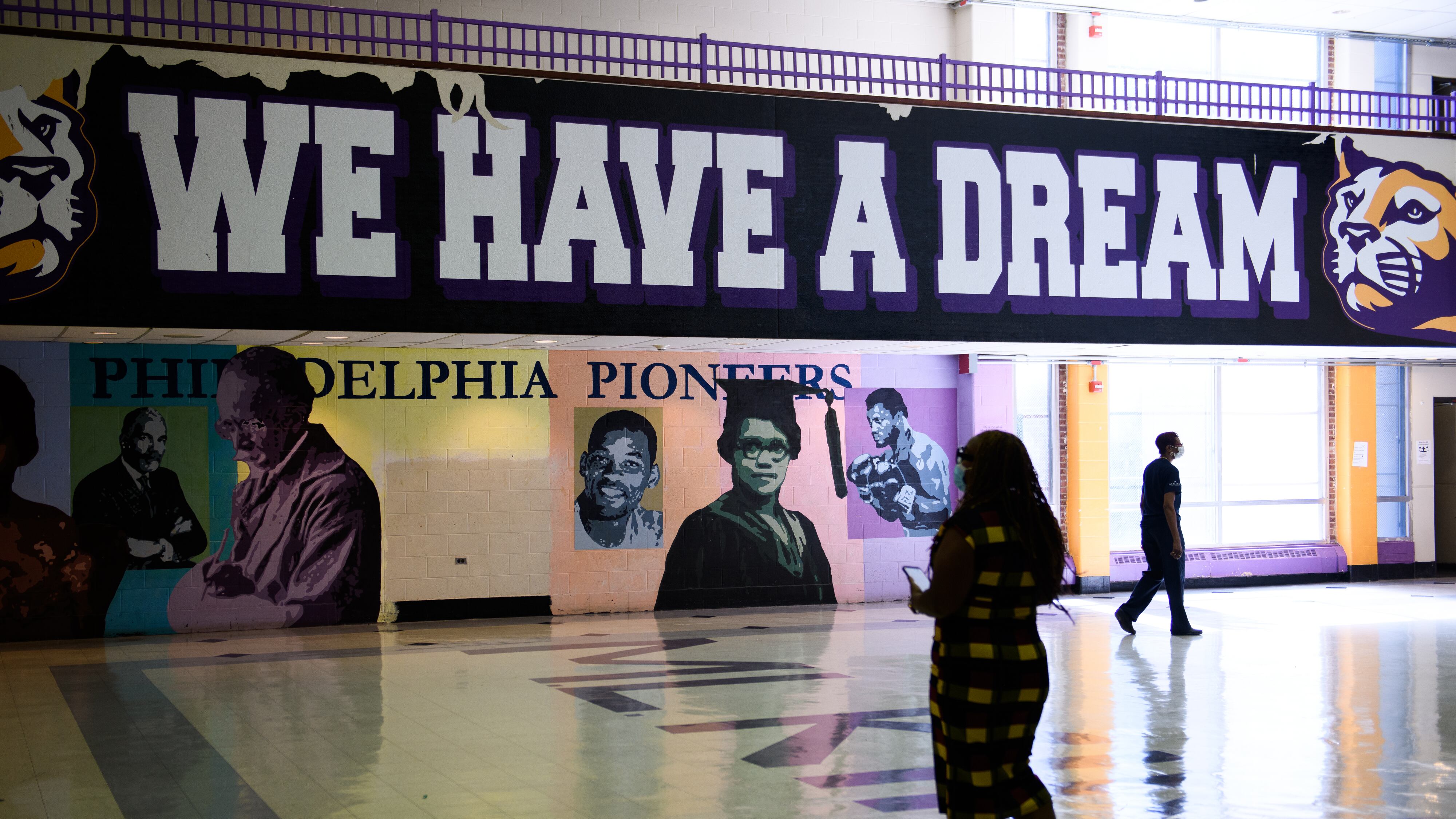 A school official walks in front of a sign in a cavernous hall that reads “We Have a Dream.”