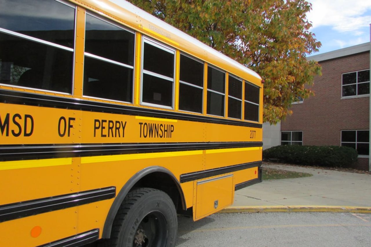 A yellow school bus with “SD of Perry Township” on the side is in front of a tree and a building.