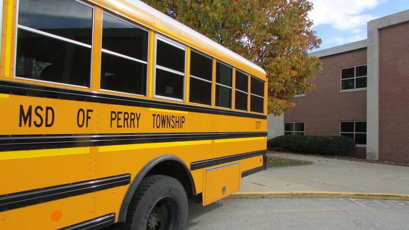 A yellow school bus with “SD of Perry Township” on the side is in front of a tree and a building.