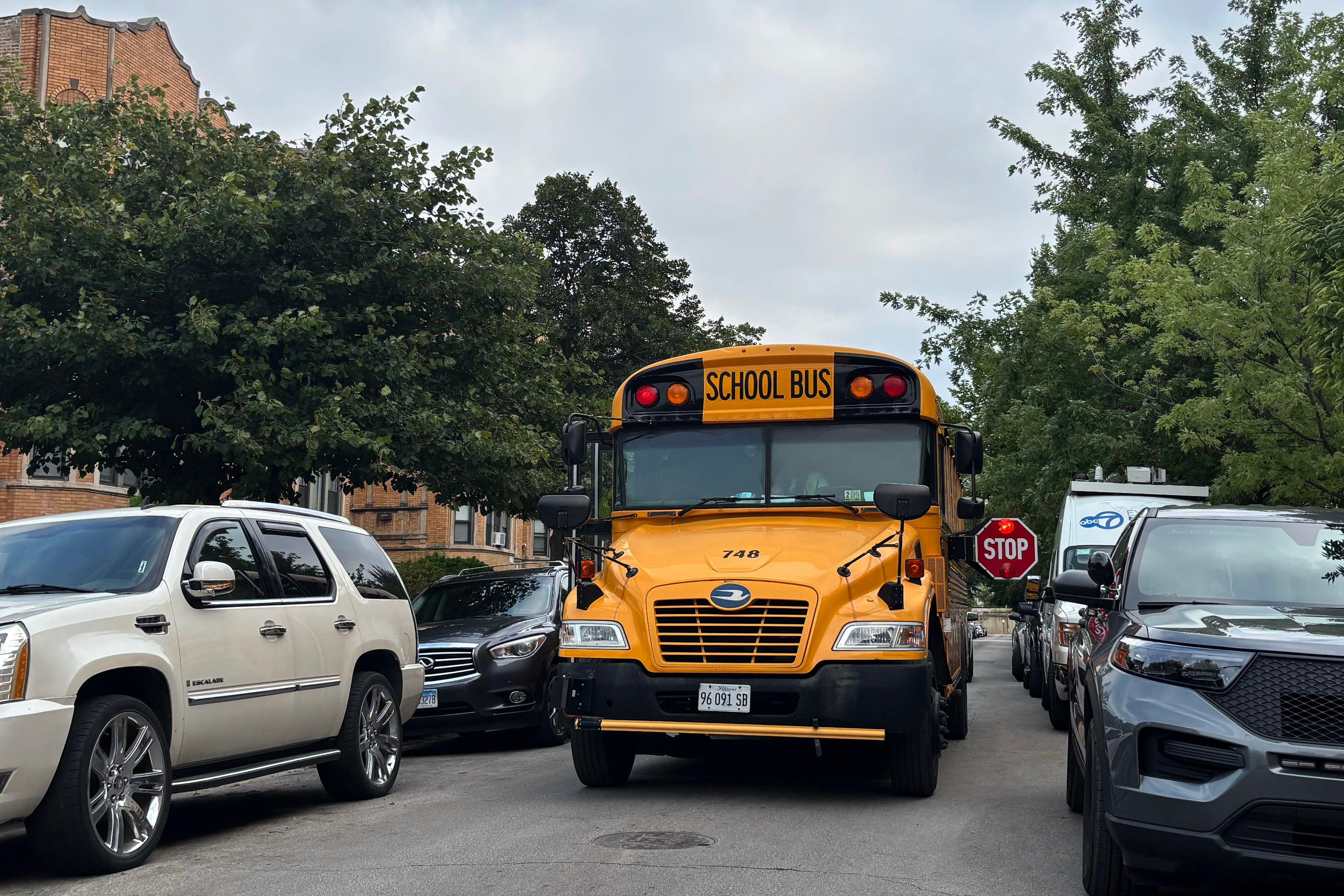 A photograph of a yellow school bus on the street with a line of cars on both sides.