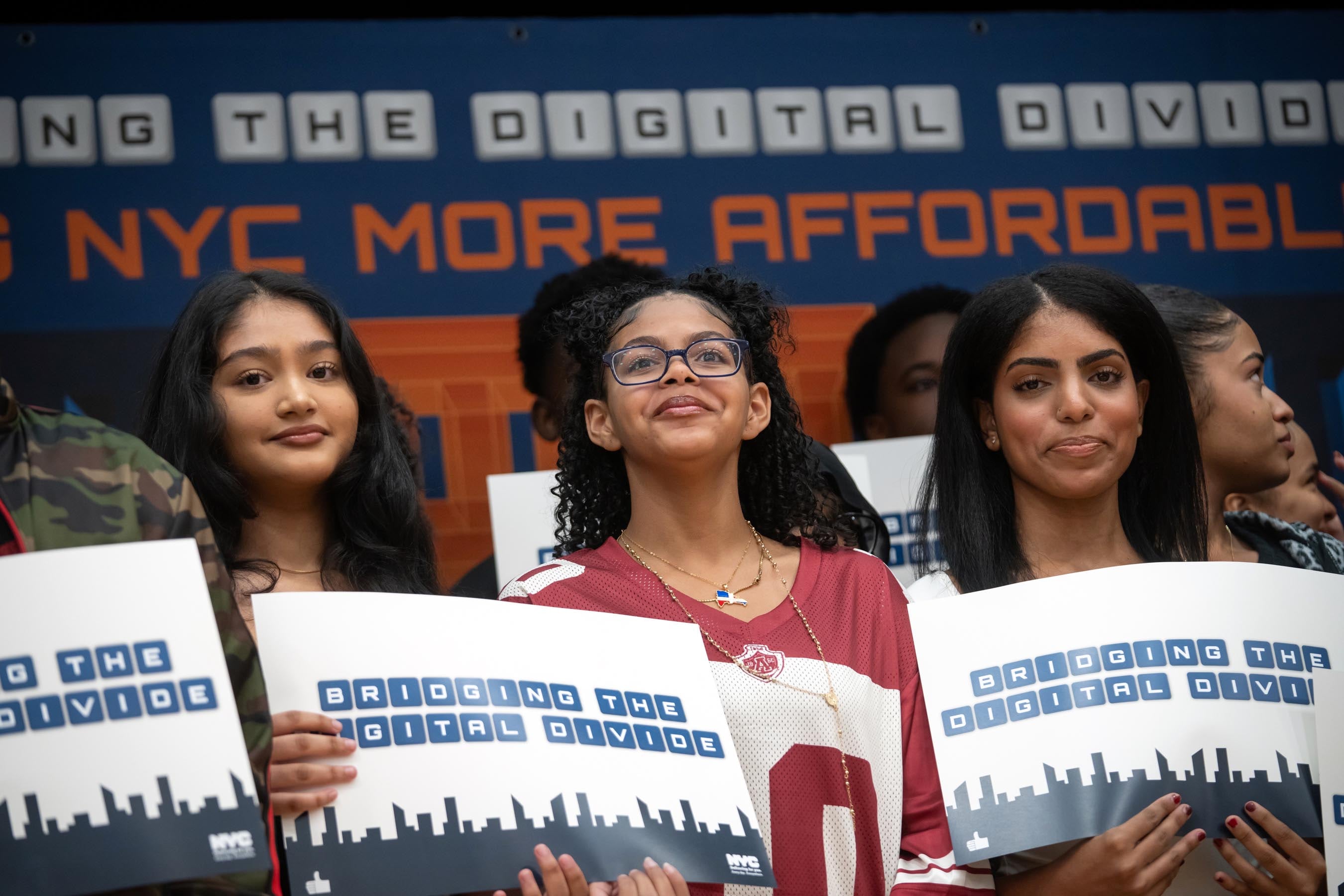 A group of teens hold signs saying "bridge the digital divide."