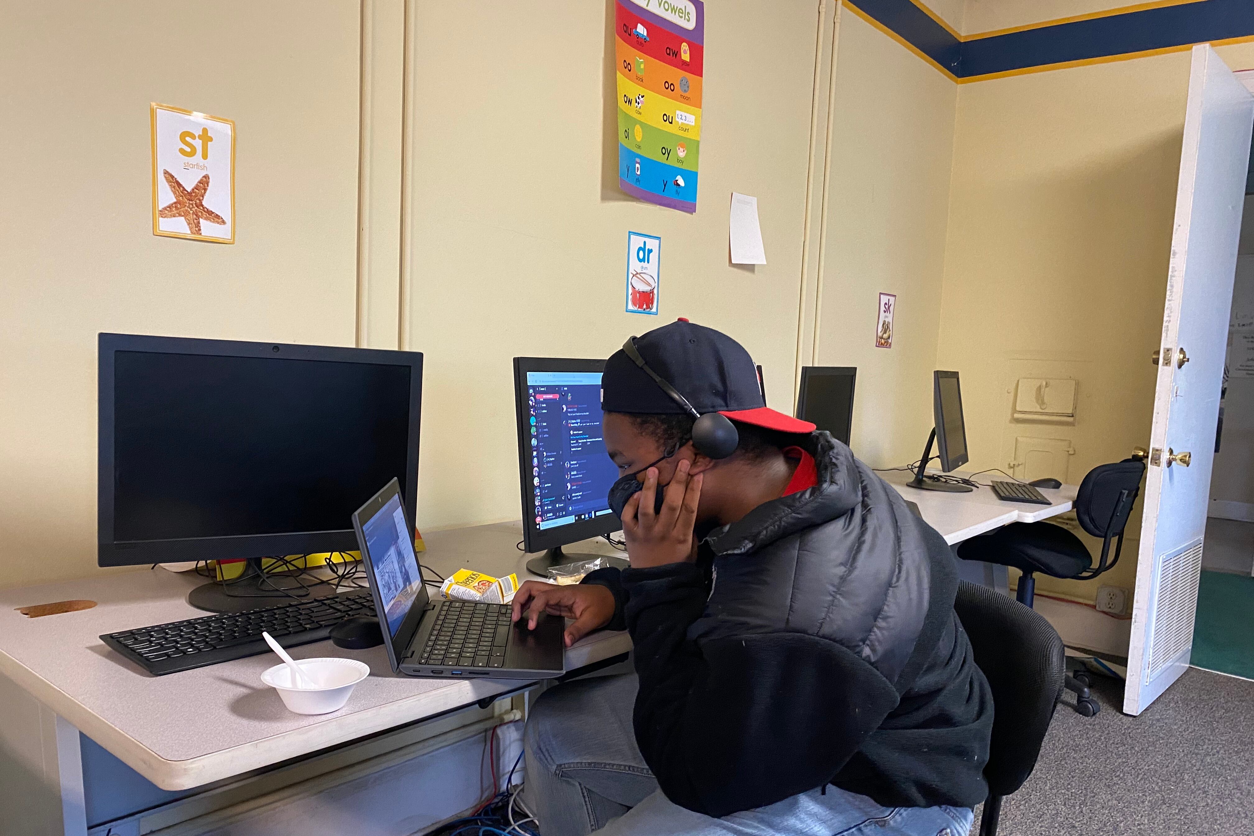 Student looks at a laptop while sitting at a table with desktop monitors