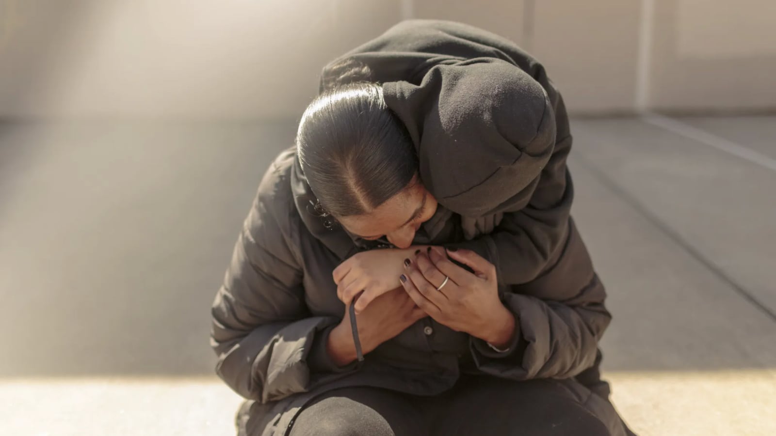 A boy wearing a hooded sweatshirt with his face obscured hugs his mom.